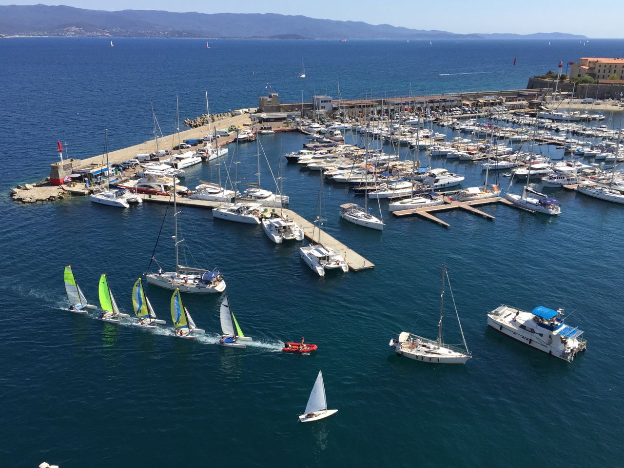 A vibrant aerial shot of Ajaccio Harbor, Corsica, showcasing sailboats on a sunny day.